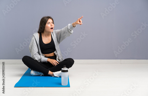 Young sport woman sitting on the floor with mat pointing away