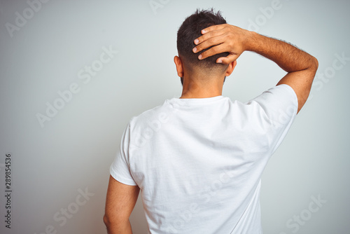 Young indian man wearing t-shirt standing over isolated white background Backwards thinking about doubt with hand on head