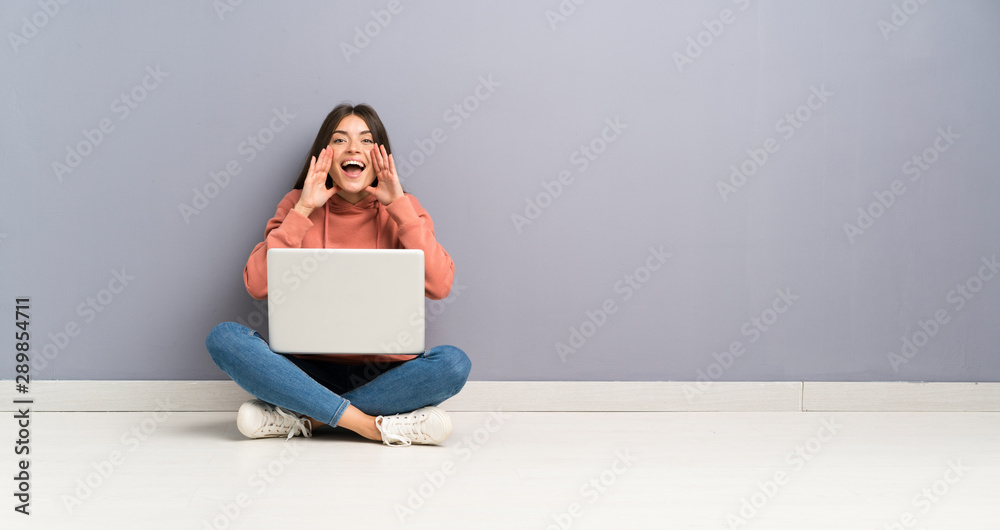 Young student girl with a laptop on the floor shouting with mouth wide open Young student girl with a laptop on the floor shouting with mouth wide open