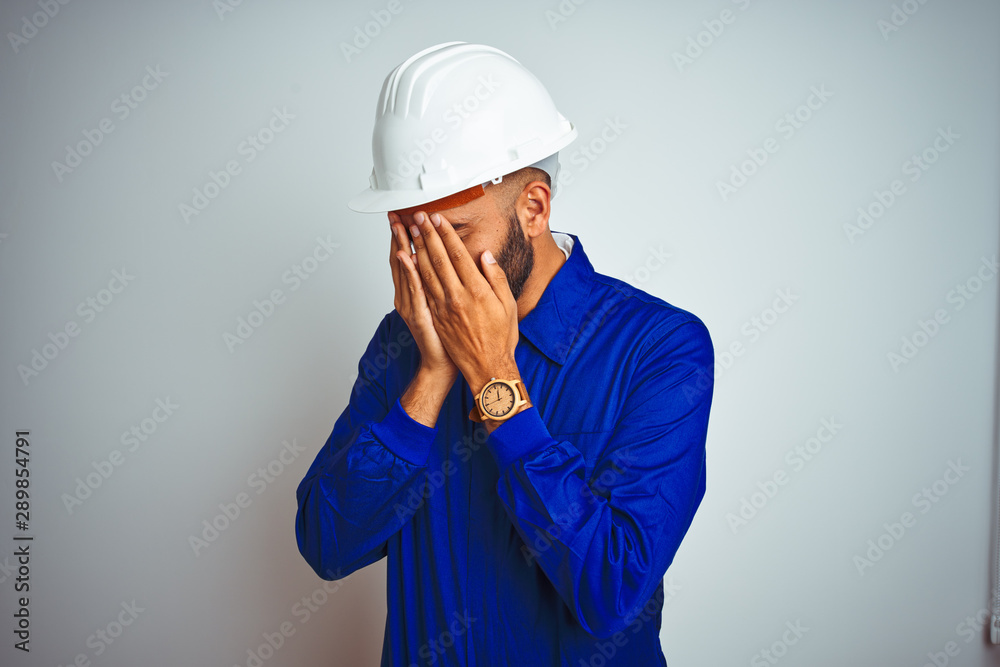 Handsome indian worker man wearing uniform and helmet over isolated white background with sad expression covering face with hands while crying. Depression concept. Handsome indian worker man wearing uniform and helmet over isolated white background with sad expression covering face with hands while crying. Depression concept.