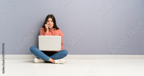 Young student girl with a laptop on the floor nervous and scared photo