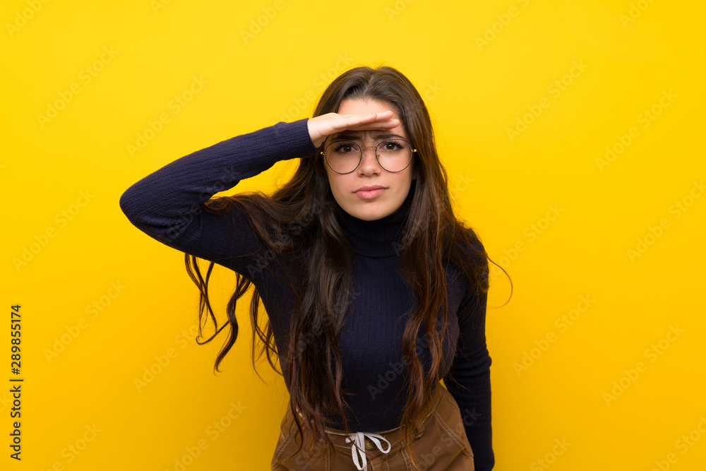 Teenager girl over isolated yellow wall looking far away with hand to look something