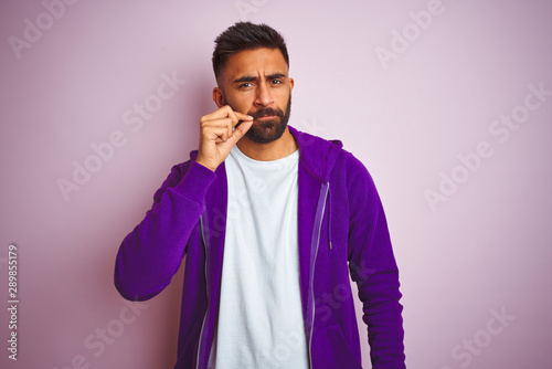 Young indian man wearing purple sweatshirt standing over isolated pink background mouth and lips shut as zip with fingers. Secret and silent, taboo talking © Krakenimages.com