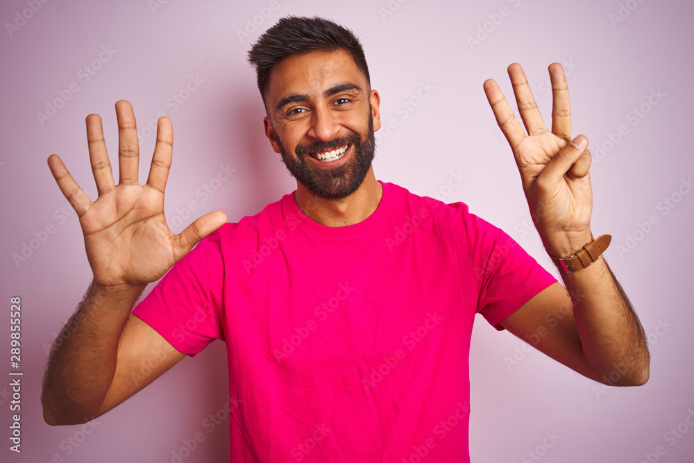 Young indian man wearing t-shirt standing over isolated pink background showing and pointing up with fingers number eight while smiling confident and happy. Young indian man wearing t-shirt standing over isolated pink background showing and pointing up with fingers number eight while smiling confident and happy.