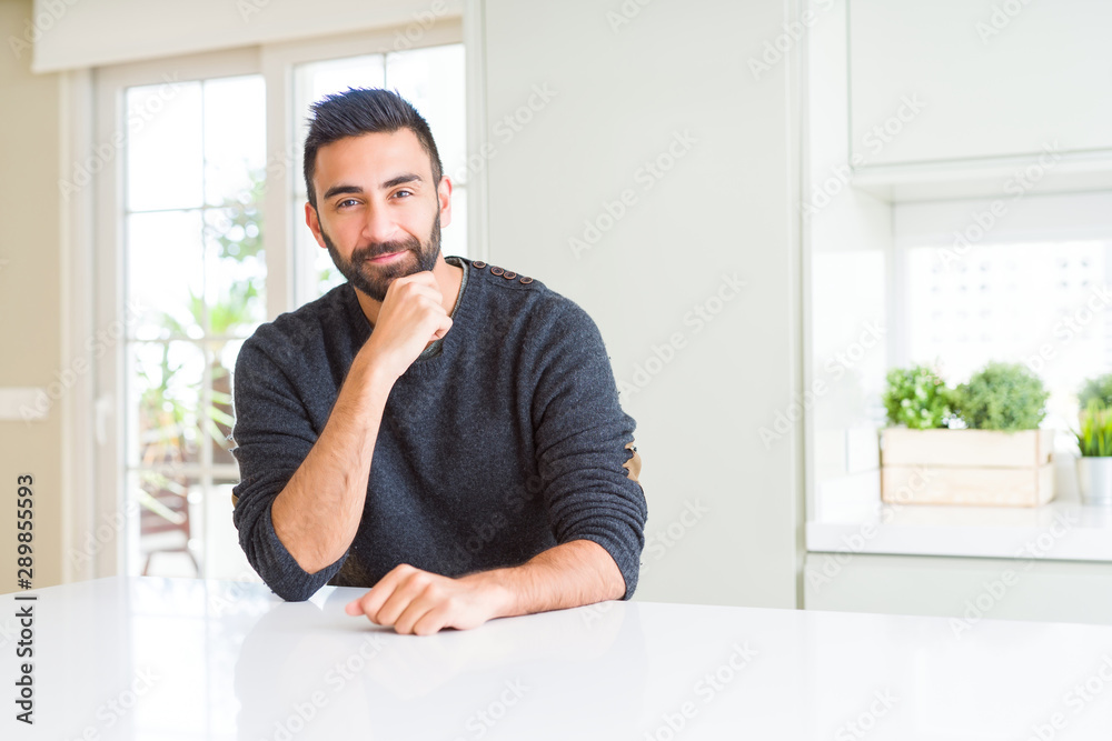 Handsome hispanic man wearing casual sweater at home looking confident at the camera with smile with crossed arms and hand raised on chin. Thinking positive. Handsome hispanic man wearing casual sweater at home looking confident at the camera with smile with crossed arms and hand raised on chin. Thinking positive.
