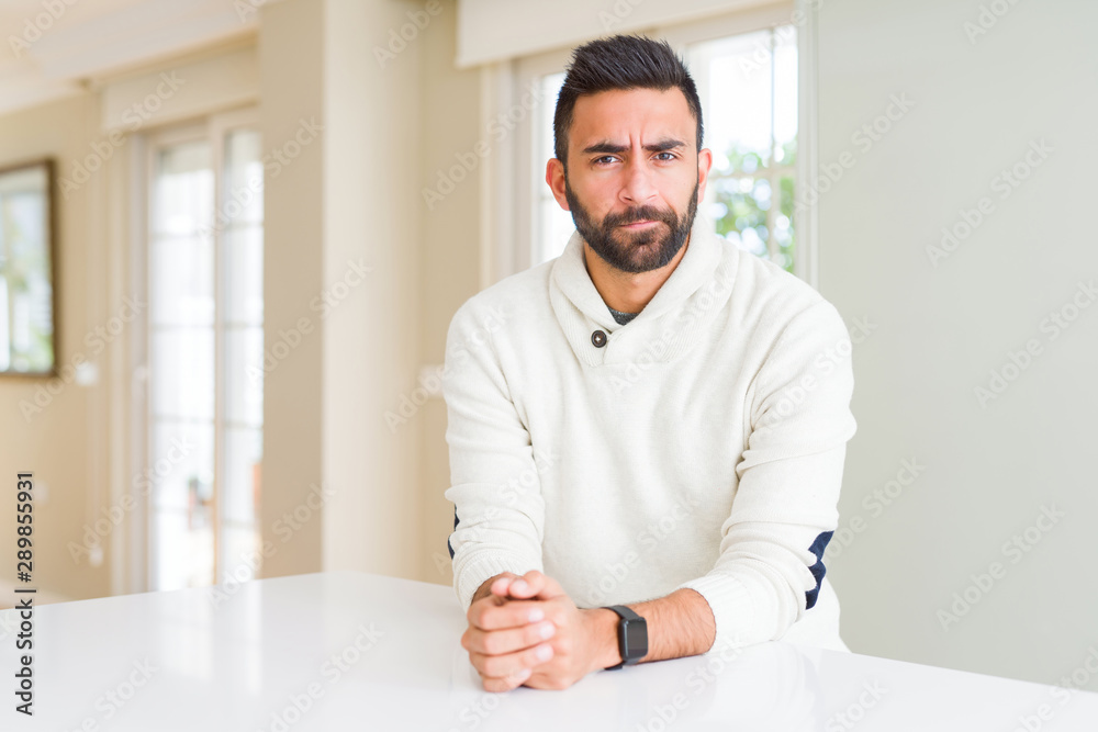 Handsome hispanic man wearing casual white sweater at home skeptic and nervous, frowning upset because of problem. Negative person.