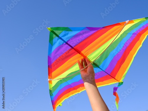  Children's hand holds a kite on a background of blue sky