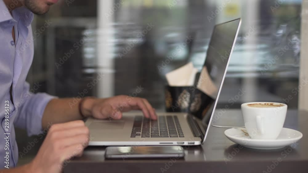 Closeup of businessman's hand keyboarding on a laptop in a coffee shop or in the office near a cup of coffee or cappuccino. Closeup of businessman's hand keyboarding on a laptop in a coffee shop or in the office near a cup of coffee or cappuccino.