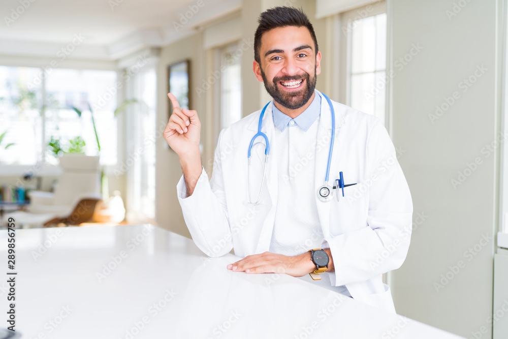 Handsome hispanic doctor man wearing stethoscope at the clinic with a big smile on face, pointing with hand and finger to the side looking at the camera. Handsome hispanic doctor man wearing stethoscope at the clinic with a big smile on face, pointing with hand and finger to the side looking at the camera.