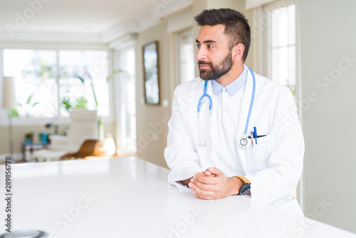 Handsome hispanic doctor man wearing stethoscope at the clinic looking to side, relax profile pose with natural face with confident smile.