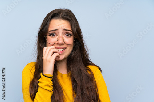 Teenager girl over isolated blue wall nervous and scared Fototapet