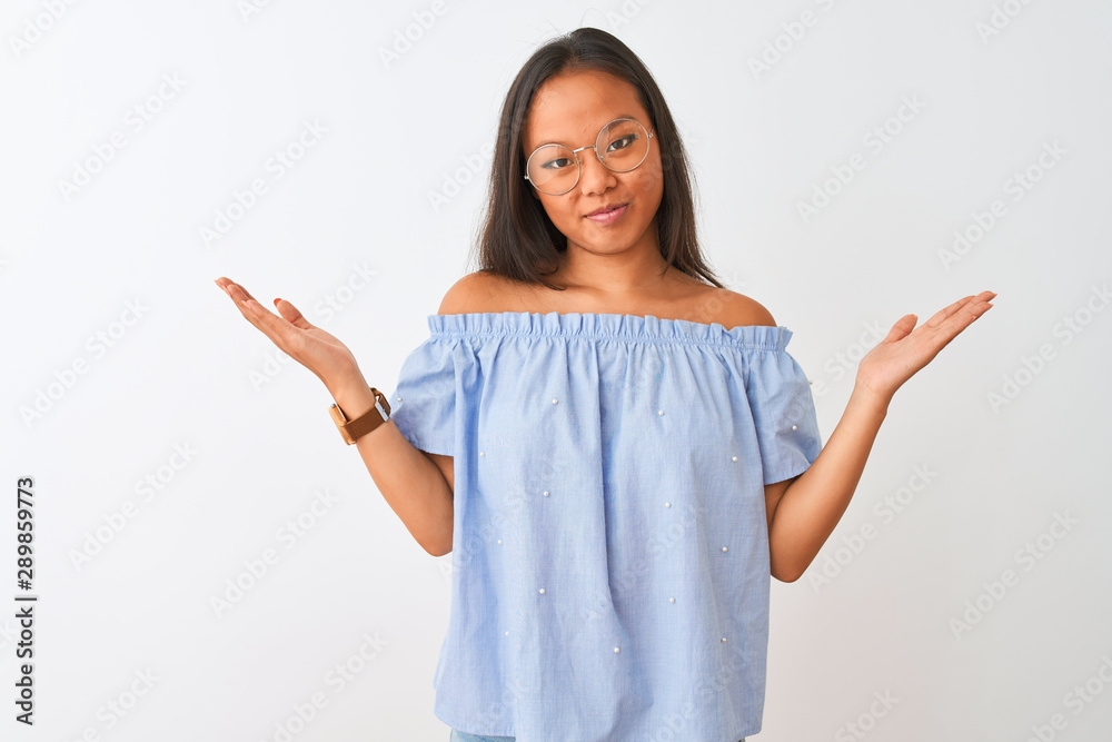 Young chinese woman wearing blue t-shirt and glasses over isolated white background clueless and confused expression with arms and hands raised. Doubt concept. Young chinese woman wearing blue t-shirt and glasses over isolated white background clueless and confused expression with arms and hands raised. Doubt concept.