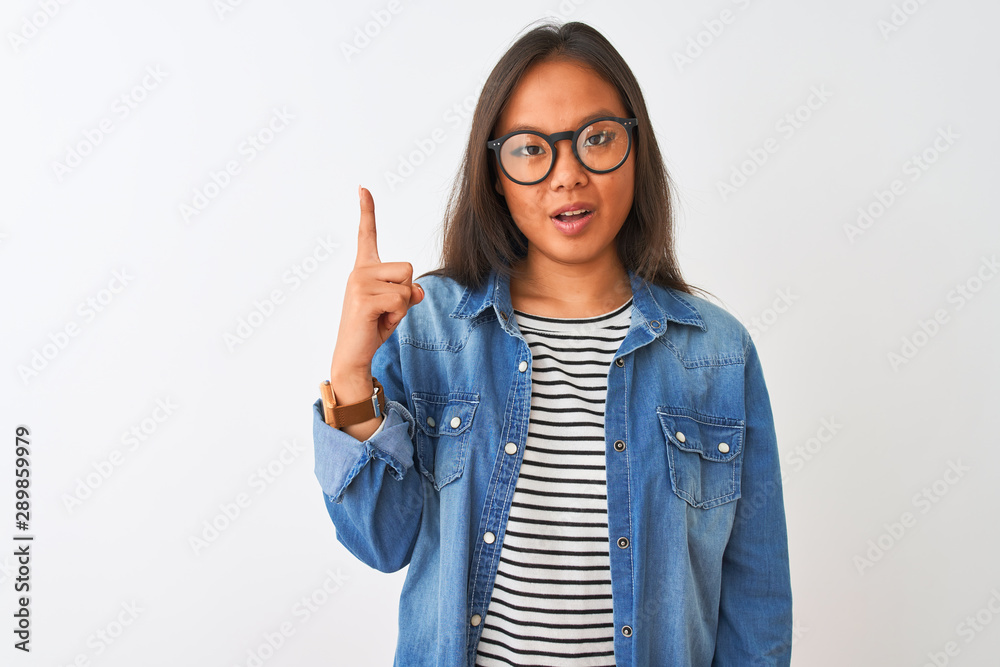 Young chinese woman wearing denim shirt and glasses over isolated white background pointing finger up with successful idea. Exited and happy. Number one. Young chinese woman wearing denim shirt and glasses over isolated white background pointing finger up with successful idea. Exited and happy. Number one.