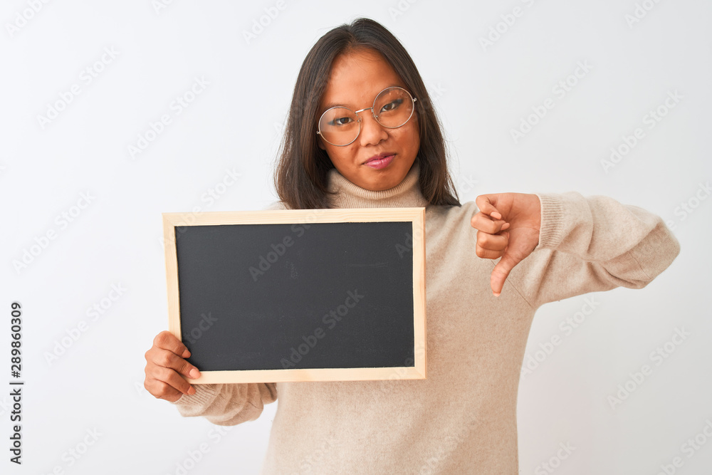 Young chinese woman wearing glasses holding blackboard over isolated white background with angry face, negative sign showing dislike with thumbs down, rejection concept Young chinese woman wearing glasses holding blackboard over isolated white background with angry face, negative sign showing dislike with thumbs down, rejection concept