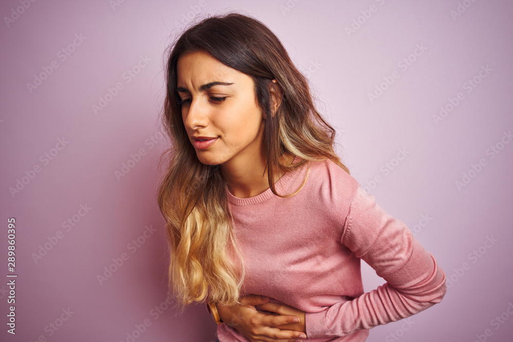 Fototapeta premium Young beautiful woman wearing a sweater over pink isolated background with hand on stomach because indigestion, painful illness feeling unwell. Ache concept.