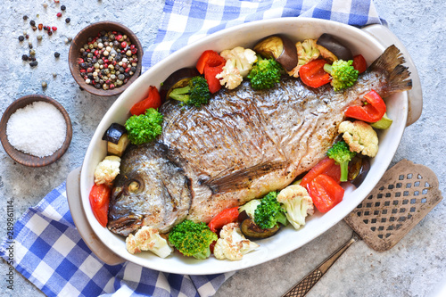 Baked dorado with different vegetables and basil on a concrete background. View from above.
