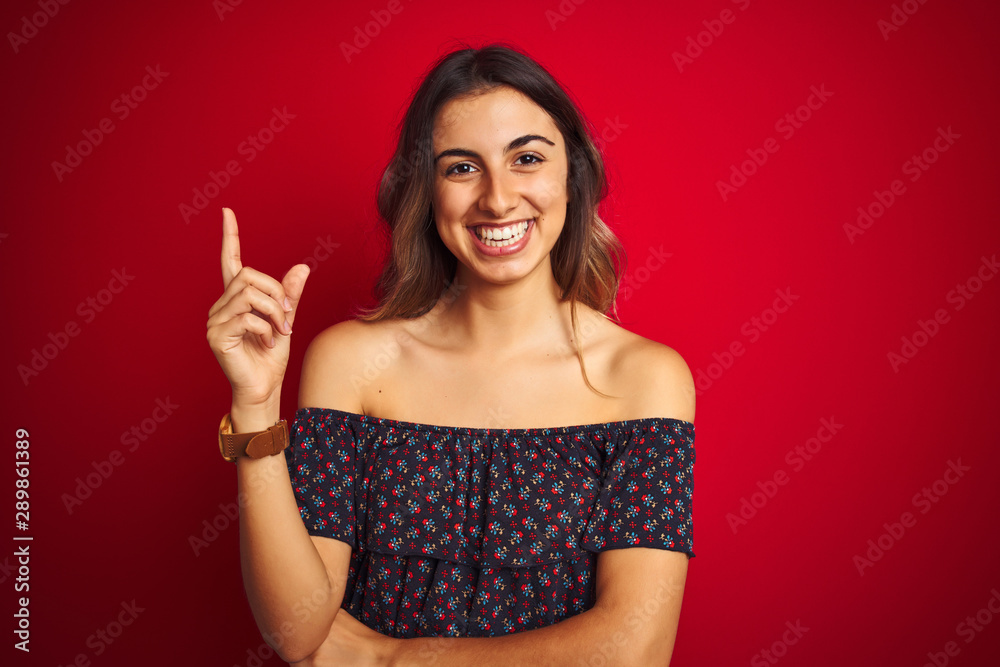 Young beautiful woman wearing a floral t-shirt over red isolated background with a big smile on face, pointing with hand and finger to the side looking at the camera. Young beautiful woman wearing a floral t-shirt over red isolated background with a big smile on face, pointing with hand and finger to the side looking at the camera.