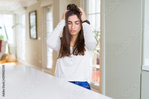 Beautiful young woman sitting on white table at home suffering from headache desperate and stressed because pain and migraine. Hands on head.