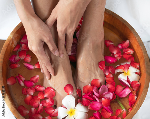 Female feet and hands in wooden bowl with flowers at spa salon.