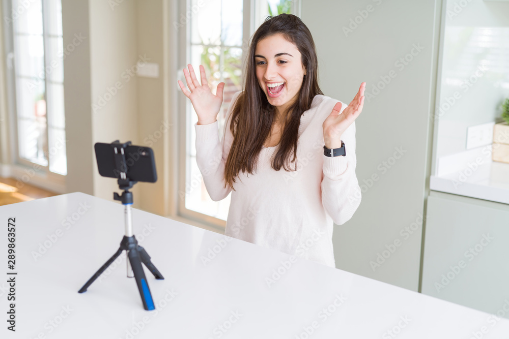 Beautiful young woman recording selfie video with smartphone webcam very happy and excited, winner expression celebrating victory screaming with big smile and raised hands