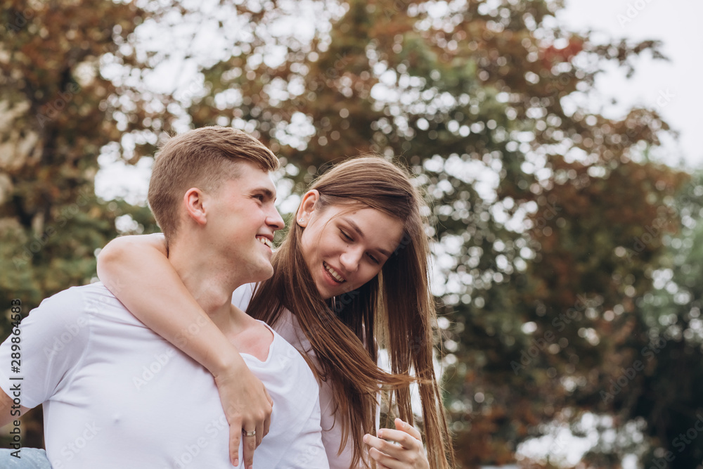 Happy young couple walks the streets of the city and hold hands. guy and girl in white t-shirts and jeans outdoors. Teenagers cuddling against the backdrop of an autumn tree. Couple close-up portrait