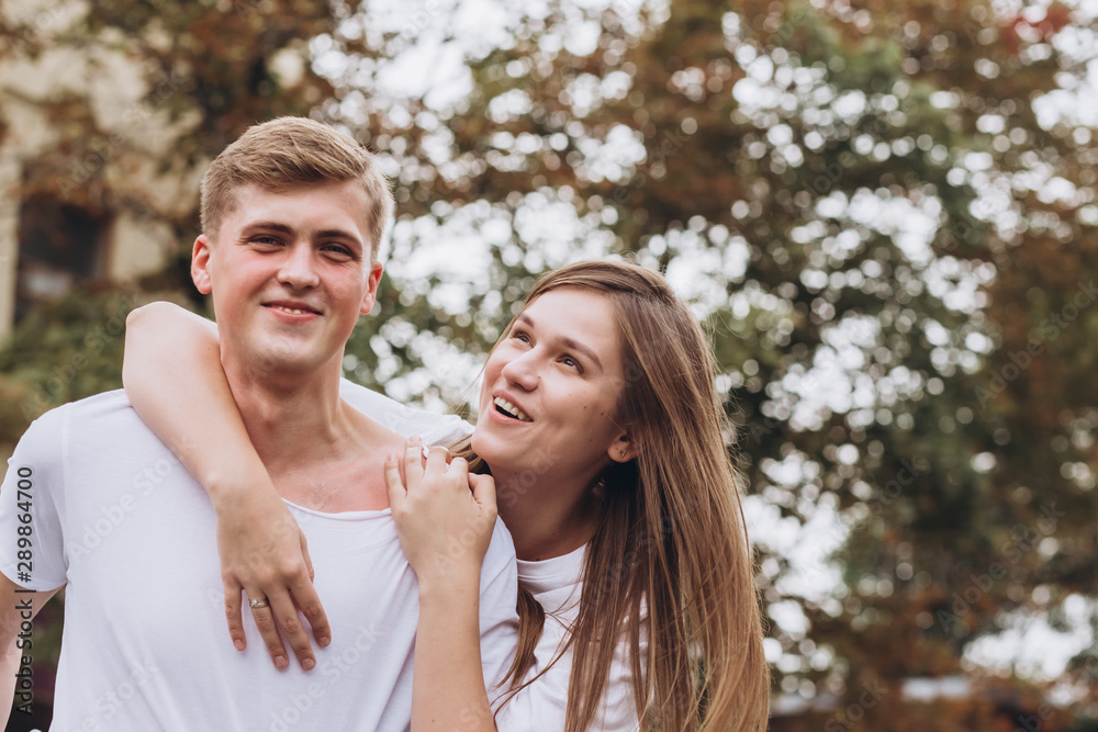Happy young couple walks the streets of the city and hold hands. guy and girl in white t-shirts and jeans outdoors. Teenagers cuddling against the backdrop of an autumn tree. Couple close-up portrait Happy young couple walks the streets of the city and hold hands. guy and girl in white t-shirts and jeans outdoors. Teenagers cuddling against the backdrop of an autumn tree. Couple close-up portrait