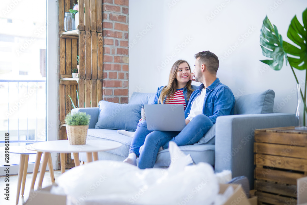 Young couple relaxing sitting on the sofa using the computer laptop around cardboard boxes, very happy moving to a new house Young couple relaxing sitting on the sofa using the computer laptop around cardboard boxes, very happy moving to a new house