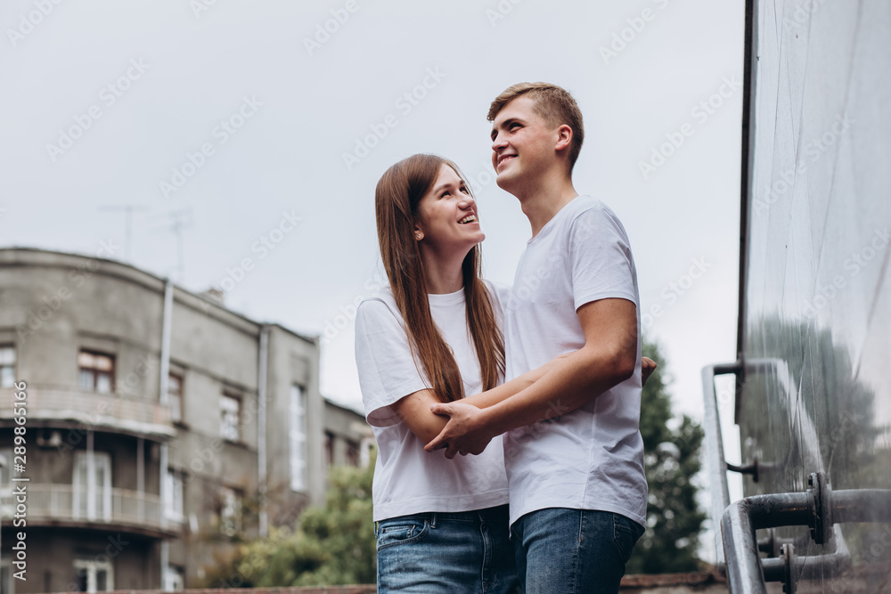Happy young couple walks the streets of the city and hold hands. guy and girl in white t-shirts and jeans outdoors. Teenagers hug on the background of the urban landscape. Couple close up portrait.