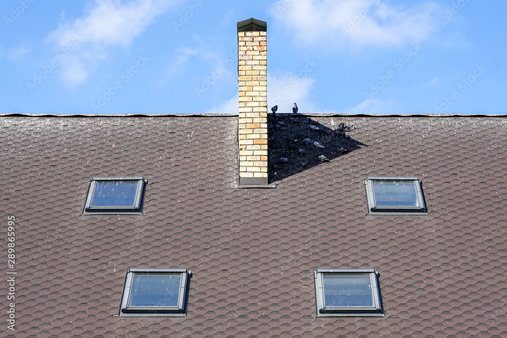 house roof with four windows and chimney, symmetrical composition against a blue sky