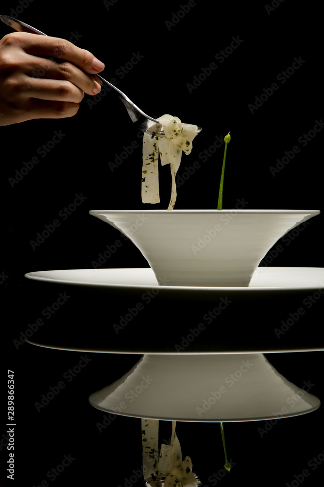 White turnip tagliatelle in a white bowl. Exquisite dish. Creative restaurant meal concept. Haute couture food on black with reflexion. Fine dining concept.