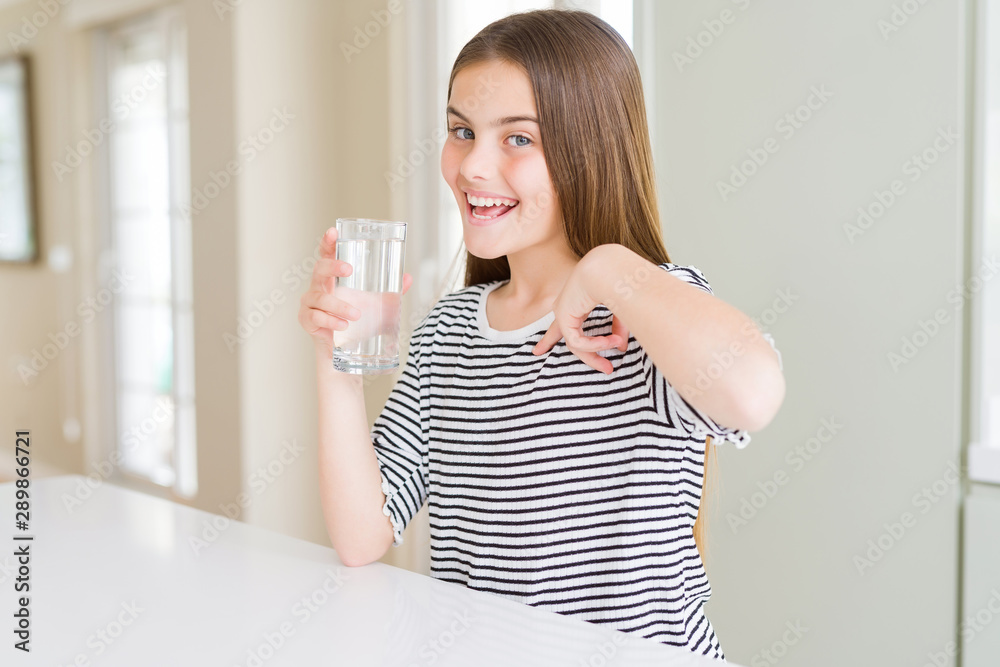Beautiful young girl kid drinking a fresh glass of water with surprise face pointing finger to himself Beautiful young girl kid drinking a fresh glass of water with surprise face pointing finger to himself