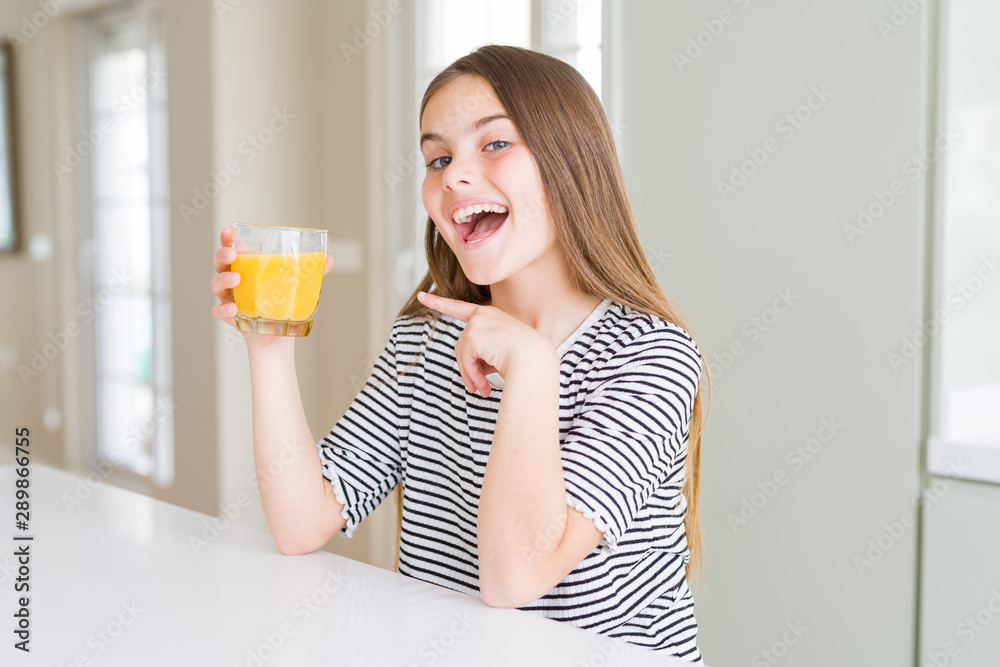 Beautiful young girl kid drinking a glass of fresh orange juice very happy pointing with hand and finger Beautiful young girl kid drinking a glass of fresh orange juice very happy pointing with hand and finger