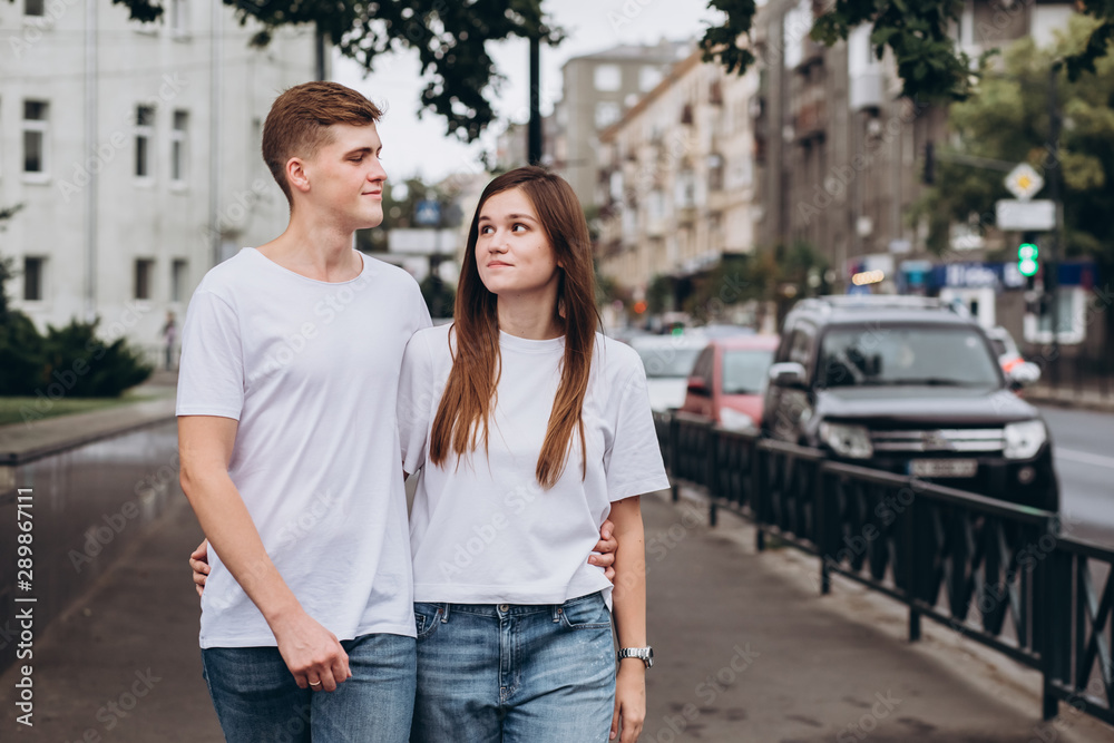 young couple walks the streets of the city and hold hands. guy and girl in white t-shirts and jeans outdoors. Teenagers walk in the autumn city. Happy young couple. young couple walks the streets of the city and hold hands. guy and girl in white t-shirts and jeans outdoors. Teenagers walk in the autumn city. Happy young couple.