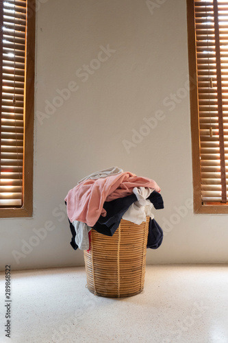 Heap of dirty clothes in wicker basket at middle of 2 windows are waiting to clean. photo