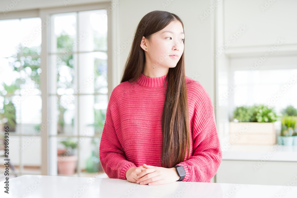 Beautiful Asian woman wearing pink sweater on white table looking to side, relax profile pose with natural face with confident smile. Beautiful Asian woman wearing pink sweater on white table looking to side, relax profile pose with natural face with confident smile.