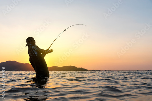 Young asian fisherman with Fishing Rod is fishing on the lake at sunset.