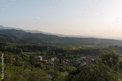 Summer in the mountains of Kazakhstan. Green fields and slopes, trees growing right on the mountains and the distant snowy peaks of the mountains. On the slopes visible houses of local residents.