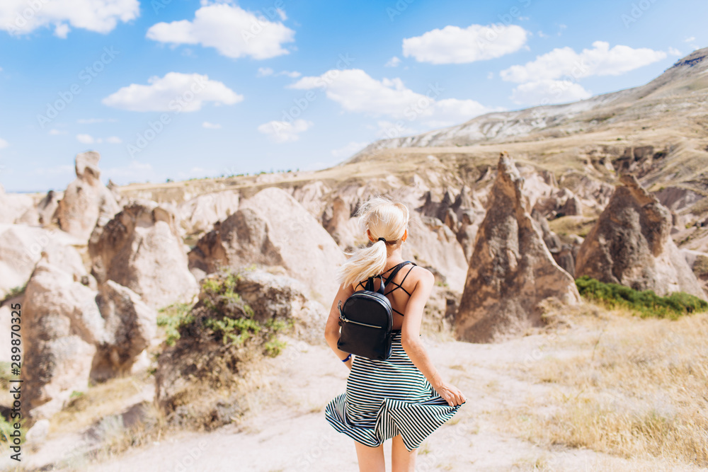 Naklejka premium A blonde girl runs across the mountains in Turkey in Cappadocia. Follow me.