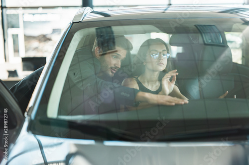 handsome man manager consulting young woman client while choosing new car in dealership
