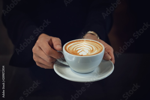 Closeup of girl hands holding white cup of latte art coffee with dark background