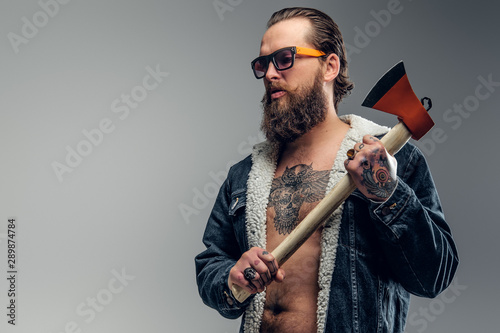 Brutal bearded man in sunglasses and denim jacket is holding axe.