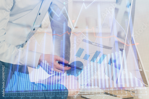 Double exposure of chart with businessman typing on computer in office on background. Concept of hard work.