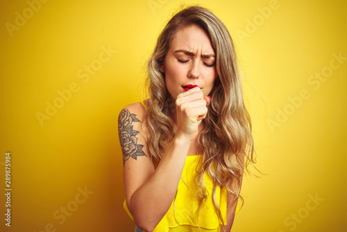 Young attactive woman wearing t-shirt standing over yellow isolated background feeling unwell and coughing as symptom for cold or bronchitis. Healthcare concept. photo