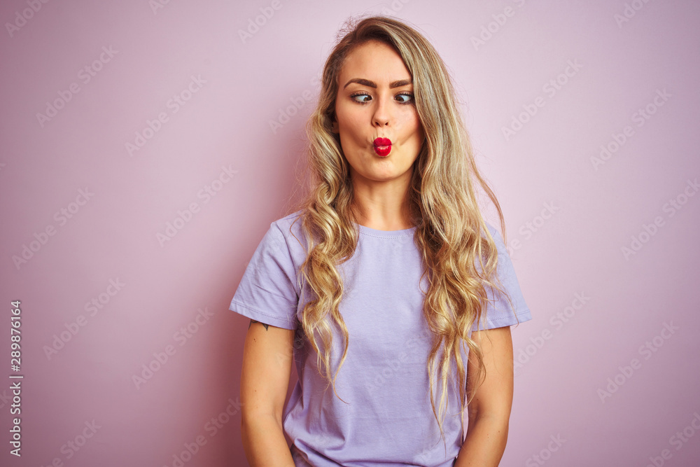 Young beautiful woman wearing purple t-shirt standing over pink isolated background making fish face with lips, crazy and comical gesture. Funny expression. Young beautiful woman wearing purple t-shirt standing over pink isolated background making fish face with lips, crazy and comical gesture. Funny expression.
