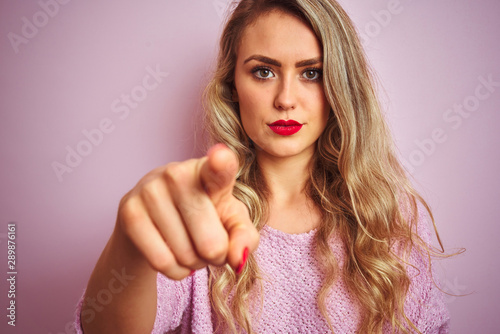 Young beautiful woman wearing sweater standing over pink isolated background pointing with finger to the camera and to you, hand sign, positive and confident gesture from the front