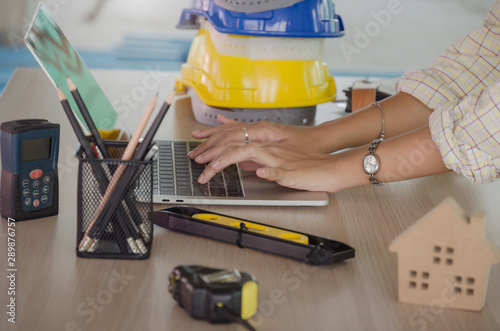 hand professional architect, engineer or interior hands working with laptop and safety helmet on workplace desk in office center at construction site, contractor, construction and engineering concept
