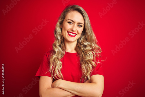 Young beautiful woman wearing basic t-shirt standing over red isolated background happy face smiling with crossed arms looking at the camera. Positive person.