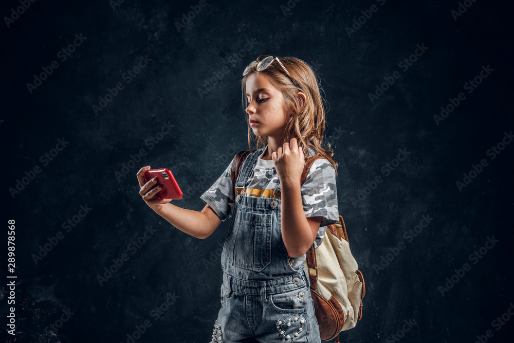 Pretty little girl is making selfie by mobile phone at dark photo studio. Pretty little girl is making selfie by mobile phone at dark photo studio.