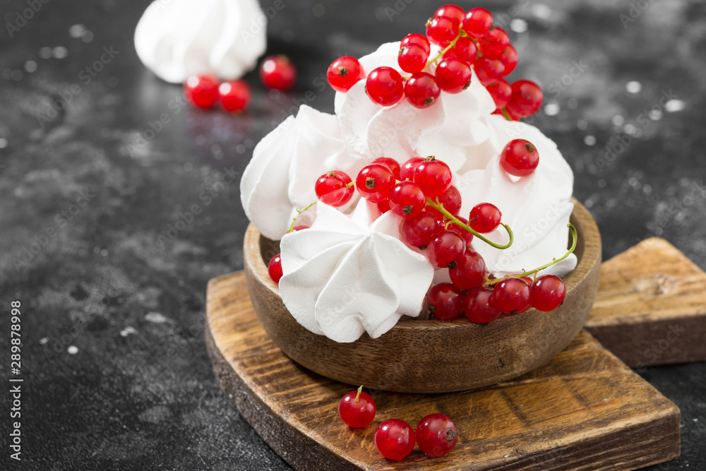 White meringue with currants in a wooden bowl on a black table. French dessert. Place for text White meringue with currants in a wooden bowl on a black table. French dessert. Place for text