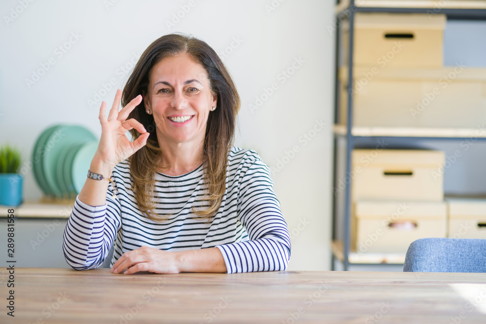 Middle age senior woman sitting at the table at home smiling positive doing ok sign with hand and fingers. Successful expression. Middle age senior woman sitting at the table at home smiling positive doing ok sign with hand and fingers. Successful expression.